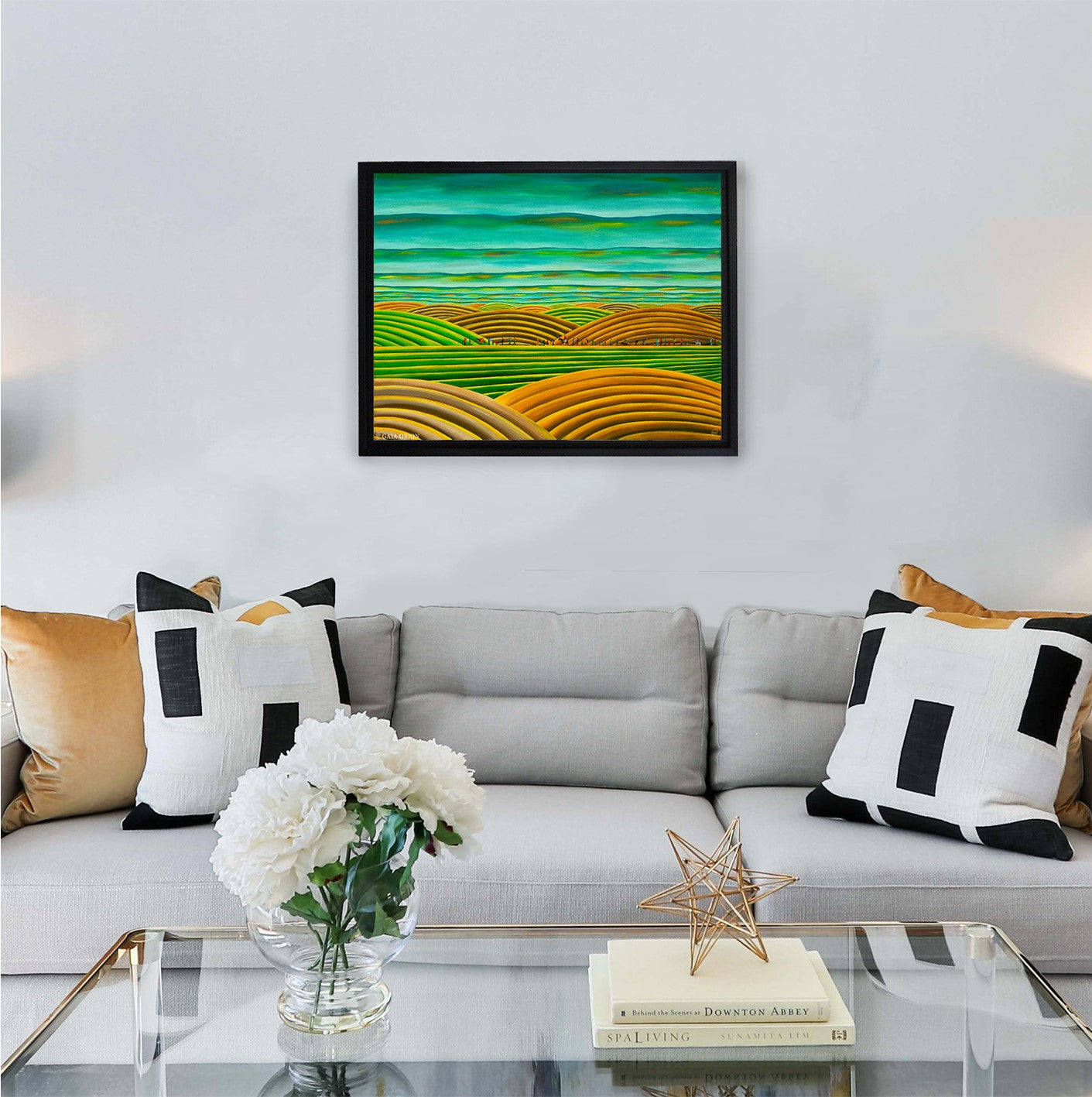 A framed print on canvas above a couch of a painting called Nomads yellow blue green sunset colours